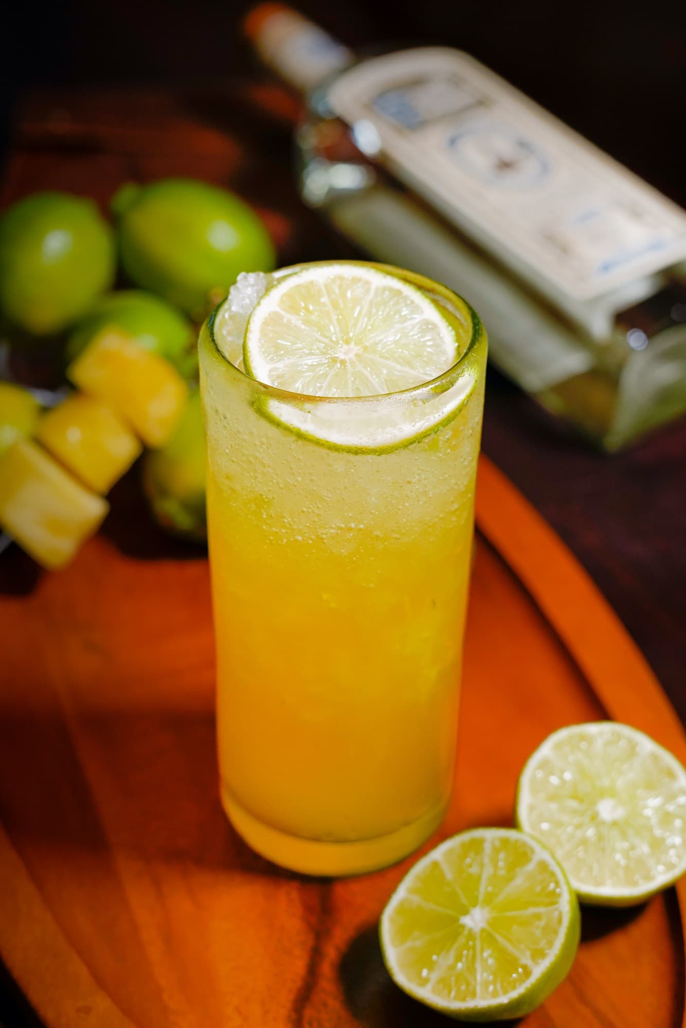 El Matador Pedro in a tall glass with a lime wheel, beside pineapple chunks, limes and a bottle of Pedro Furtivo Blanco on a wooden tray