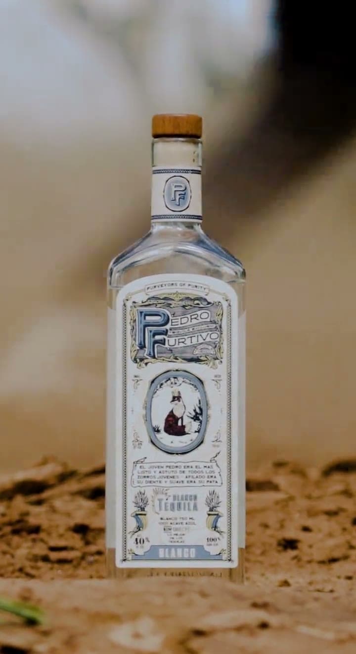 A bottle of Pedro Furtivo Blanco standing in the dirt as a horse walks past