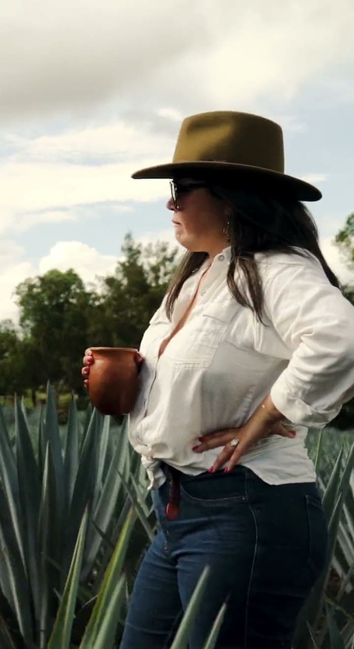 A woman in a wide-brimmed hat standing in the agave field, then two people walking the rows