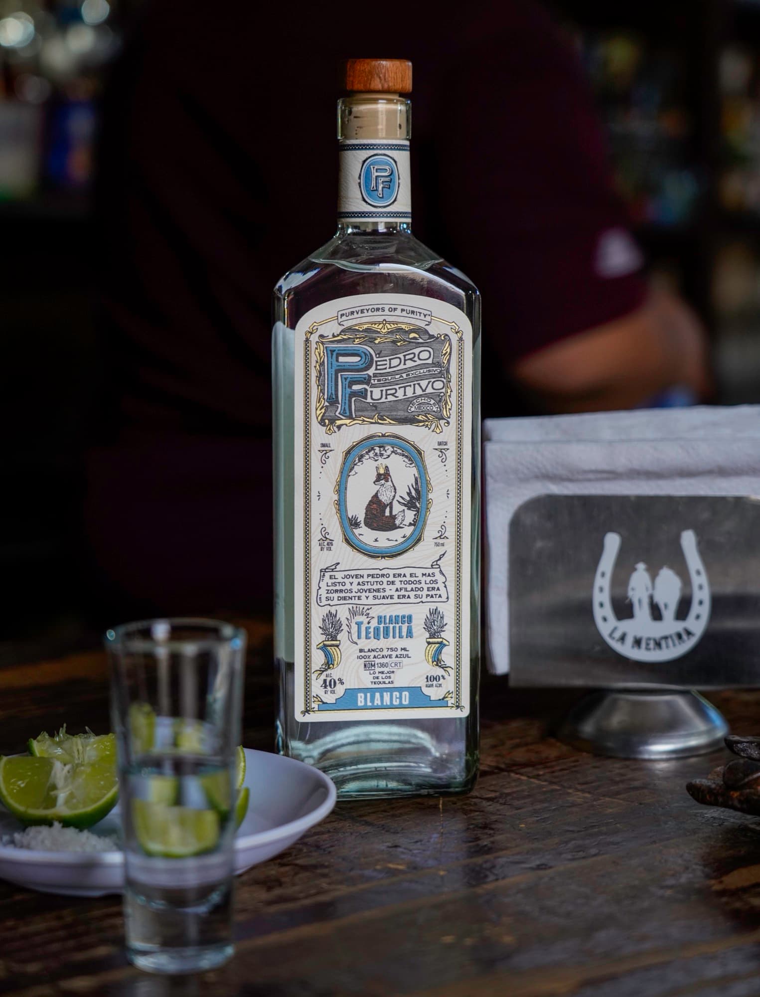 Pedro Furtivo Blanco on a bar beside a shot glass and lime wedges