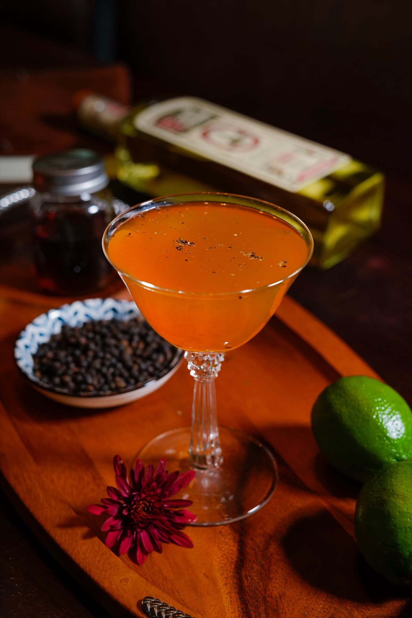 An orange Paco’s Pimiento Dulce in a coupe beside black peppercorns and limes