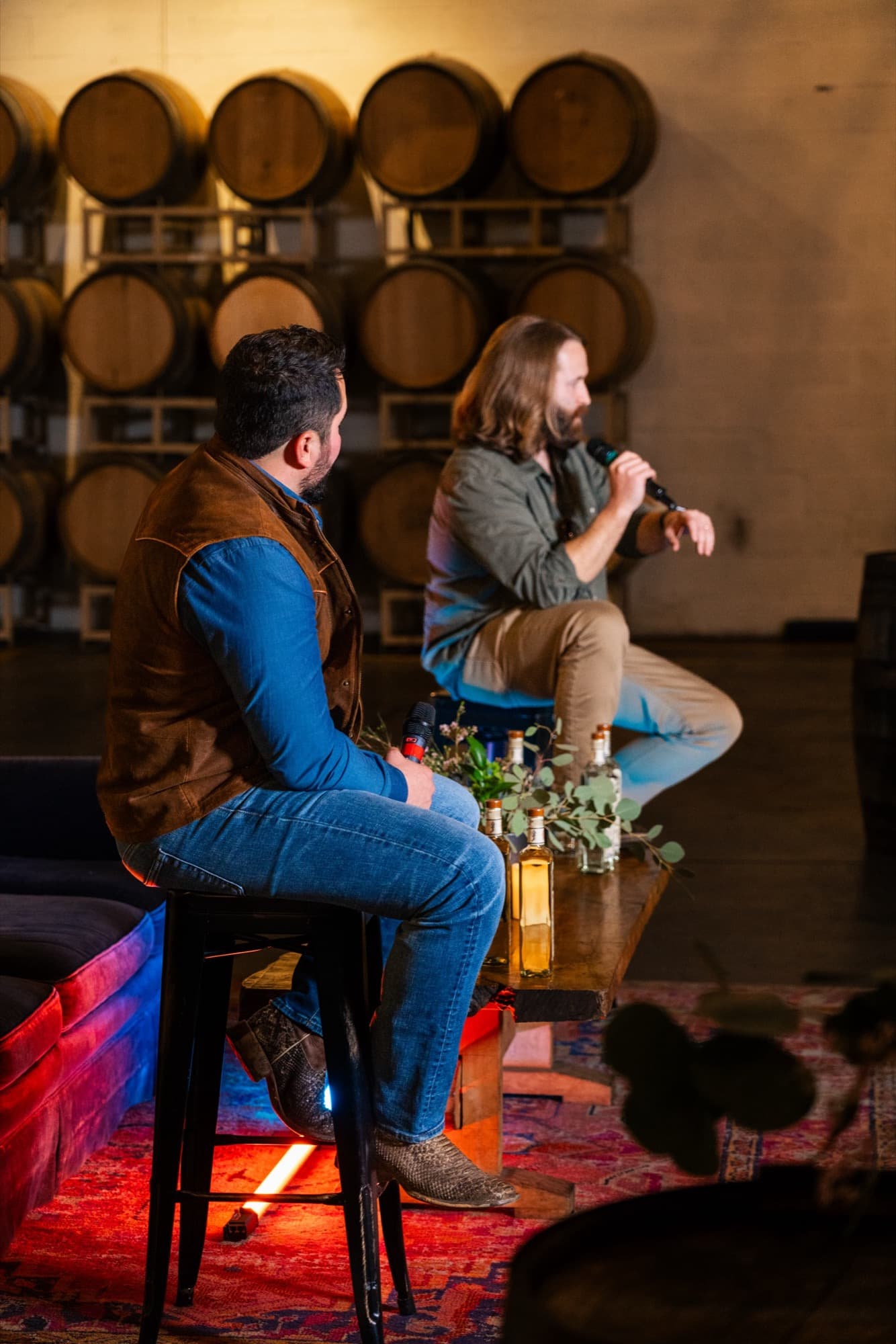 Two speakers on stools in a barrel-lined room at the Origin Story premiere