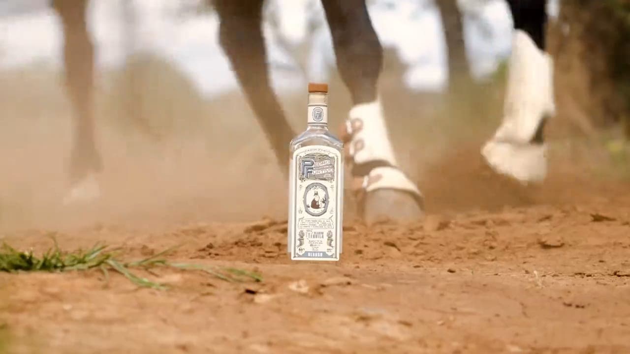 Horses’ hooves kicking up red soil beside a bottle of Pedro Furtivo Blanco