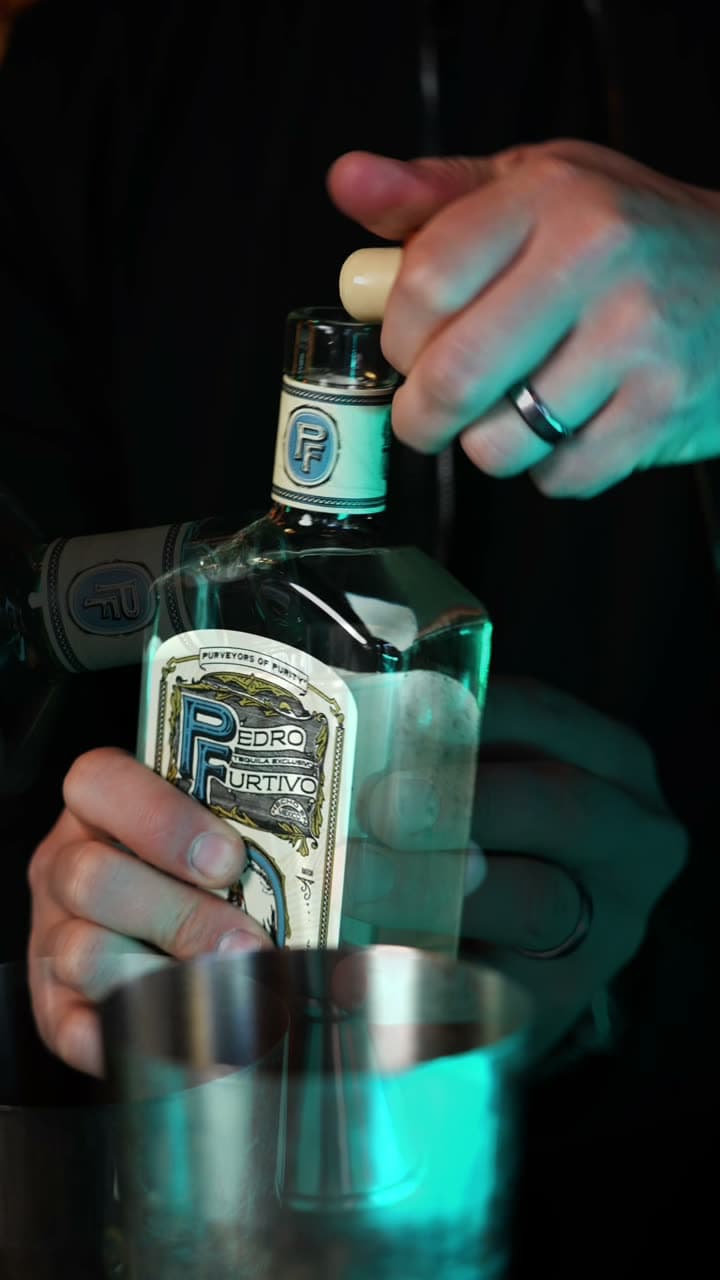 A bartender holds a bottle of Pedro Furtivo Blanco over a cocktail shaker