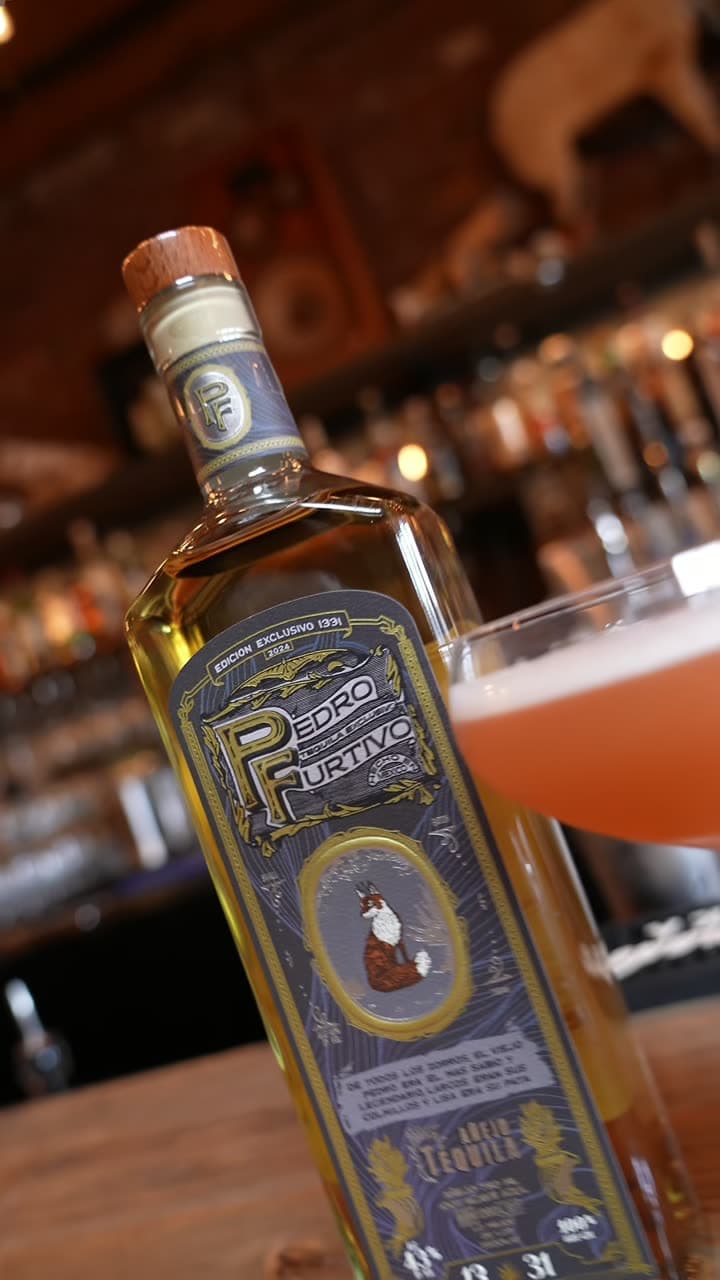 A bottle of Pedro Furtivo Añejo beside a pink cocktail on the bar at Two Birds Taphouse